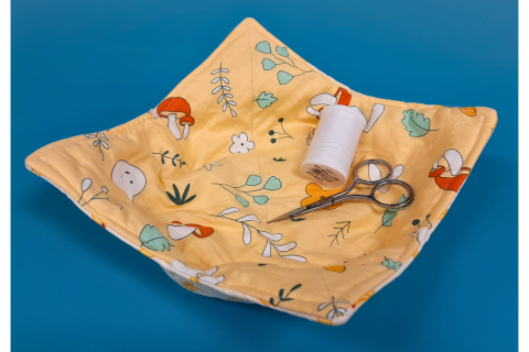 A yellow patterned fabric bowl cozy with a pair of scissors and a spool of thread. 