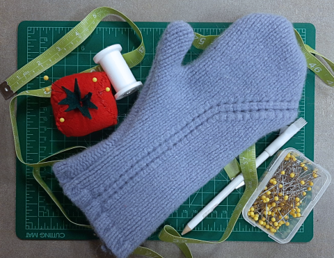 a single blue mitten surrounded by sewing supplies. 