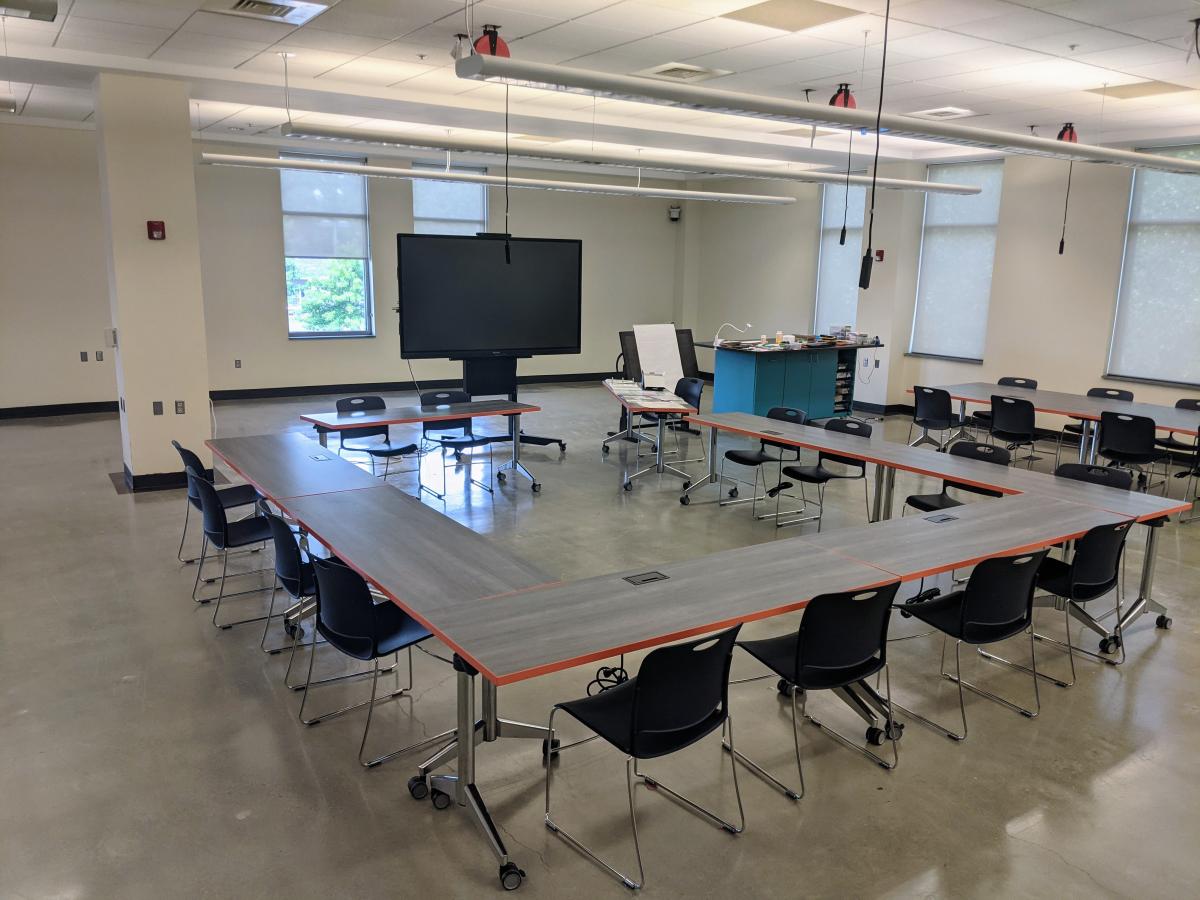 Three tables set up in a U shape with chairs facing a large Smartboard TV/computer